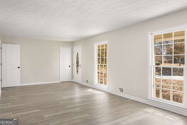 unfurnished room with a wealth of natural light, wood finished floors, visible vents, and baseboards