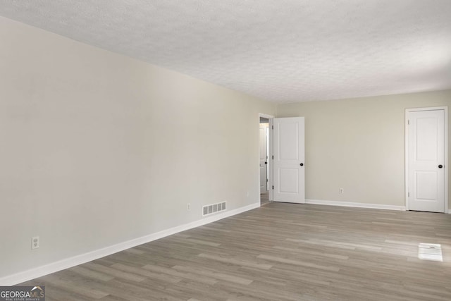 empty room with visible vents, a textured ceiling, baseboards, and wood finished floors