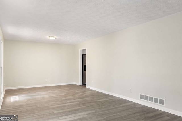 empty room with a textured ceiling, wood finished floors, visible vents, and baseboards