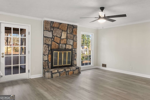 unfurnished living room with a stone fireplace, wood finished floors, visible vents, baseboards, and crown molding