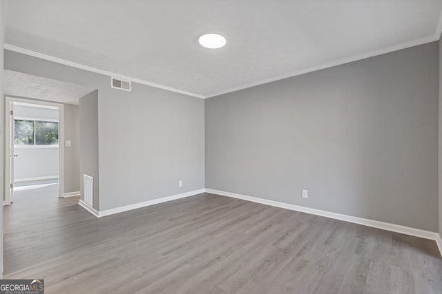 empty room with ornamental molding, wood finished floors, visible vents, and baseboards