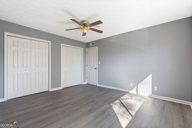 unfurnished bedroom with two closets, visible vents, ceiling fan, wood finished floors, and baseboards