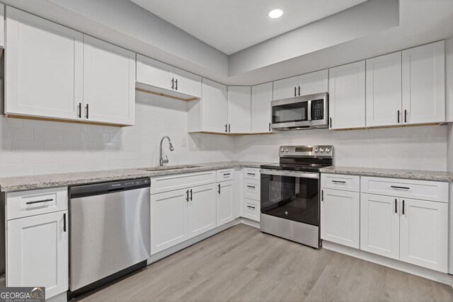 kitchen featuring a sink, white cabinets, light wood-style floors, appliances with stainless steel finishes, and tasteful backsplash