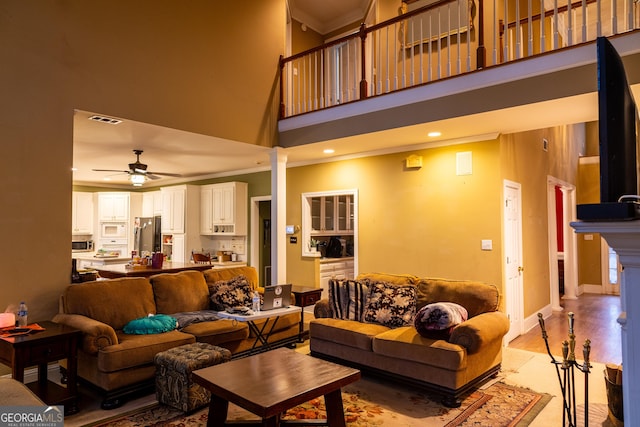 living area featuring visible vents, a ceiling fan, light wood-style flooring, ornamental molding, and ornate columns