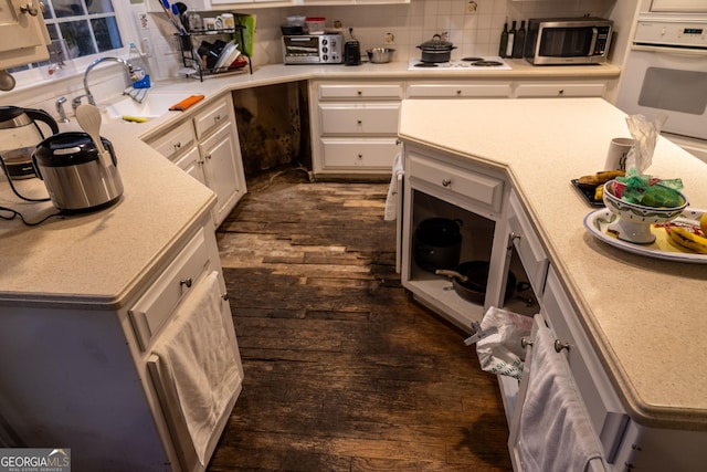 kitchen featuring dark wood-type flooring, white appliances, backsplash, and a sink