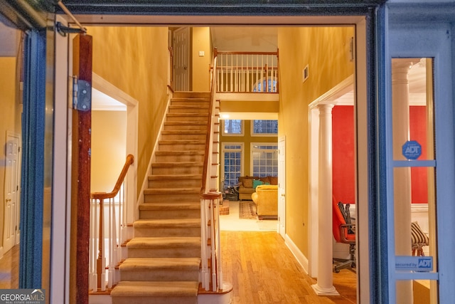 stairway with a towering ceiling, decorative columns, and wood finished floors