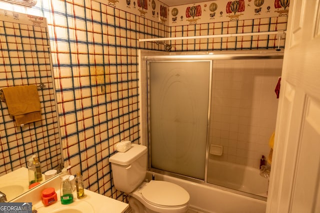 bathroom featuring wallpapered walls, toilet, combined bath / shower with glass door, vanity, and tile walls