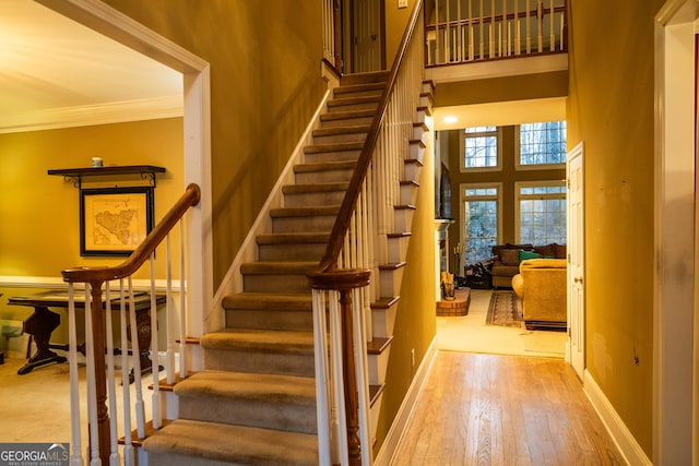 stairs with ornamental molding, wood finished floors, a towering ceiling, and baseboards