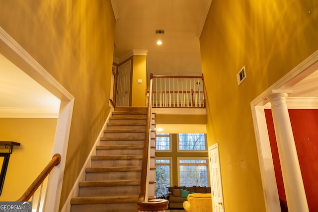 staircase featuring visible vents, crown molding, a towering ceiling, and ornate columns