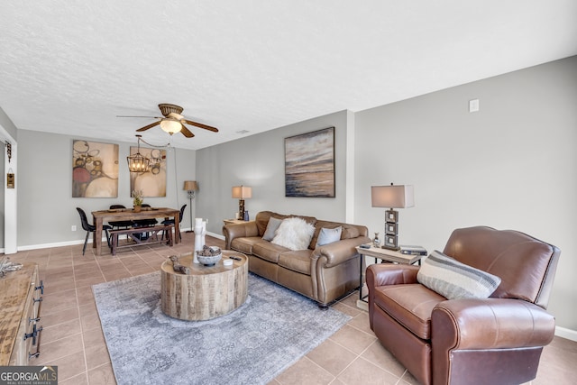 living area featuring light tile patterned floors, a textured ceiling, ceiling fan with notable chandelier, and baseboards