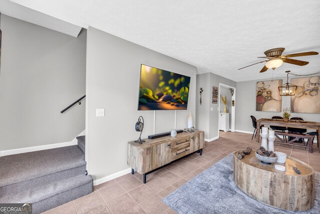 tiled living area featuring a textured ceiling, stairway, ceiling fan with notable chandelier, and baseboards