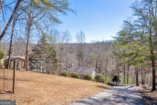 exterior space with an outdoor structure, a wooded view, and a storage unit