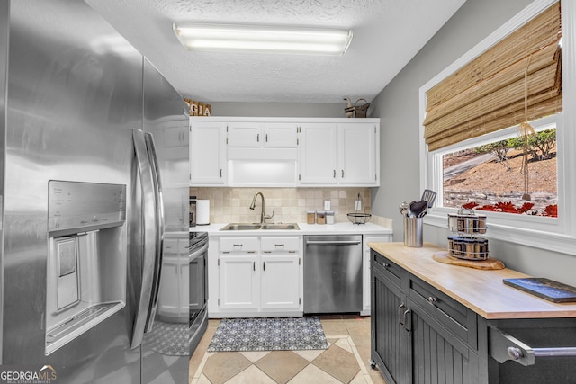 kitchen featuring white cabinets, a sink, stainless steel appliances, a textured ceiling, and backsplash