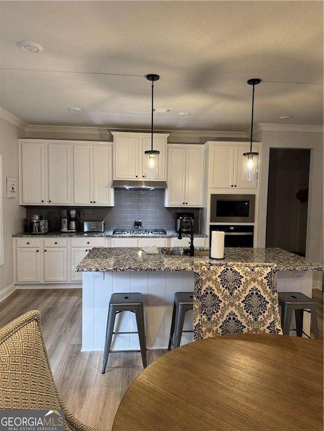 kitchen with stainless steel appliances, ornamental molding, a breakfast bar, and under cabinet range hood