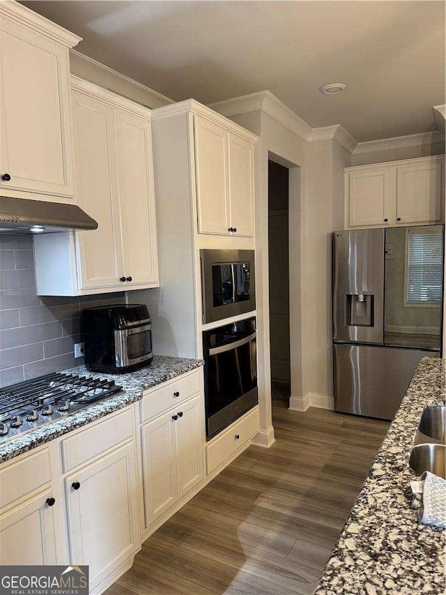 kitchen with stainless steel appliances, light stone counters, decorative backsplash, and under cabinet range hood