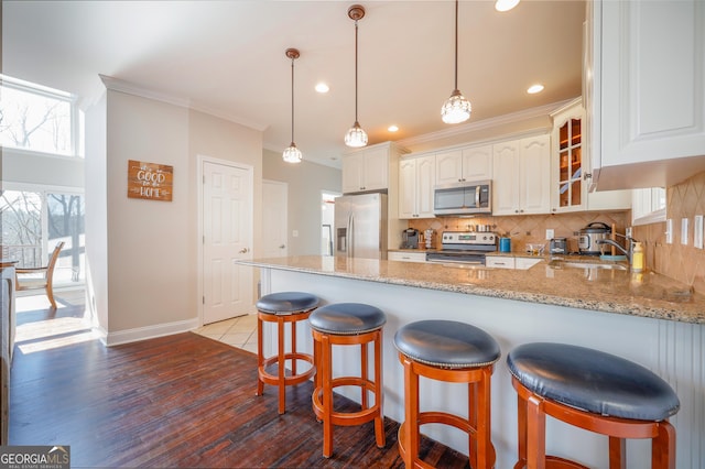 kitchen with stainless steel appliances, a peninsula, backsplash, light stone countertops, and crown molding