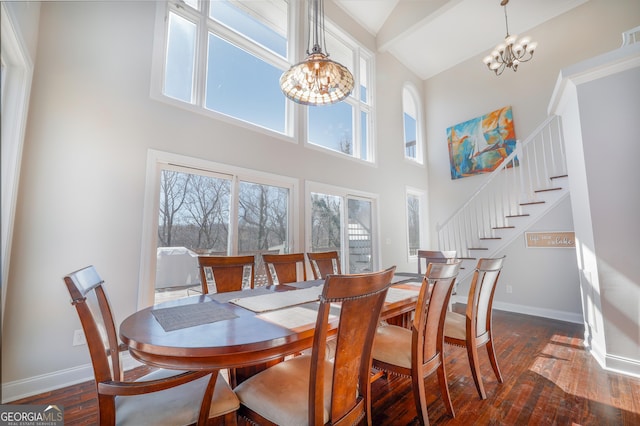 dining area featuring a towering ceiling, dark wood-type flooring, a chandelier, baseboards, and stairs