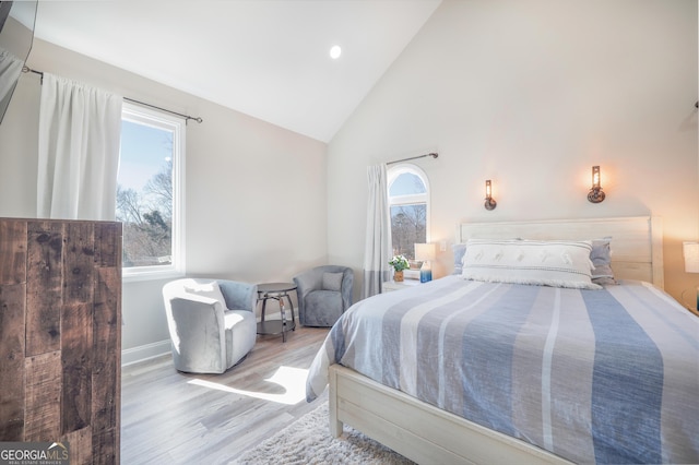 bedroom featuring high vaulted ceiling, multiple windows, baseboards, and wood finished floors