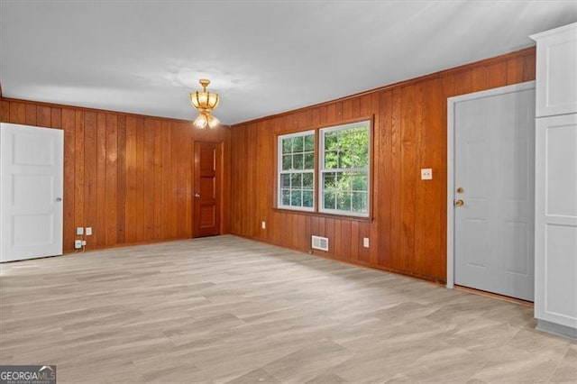 unfurnished living room with wood walls, light wood-style flooring, and visible vents