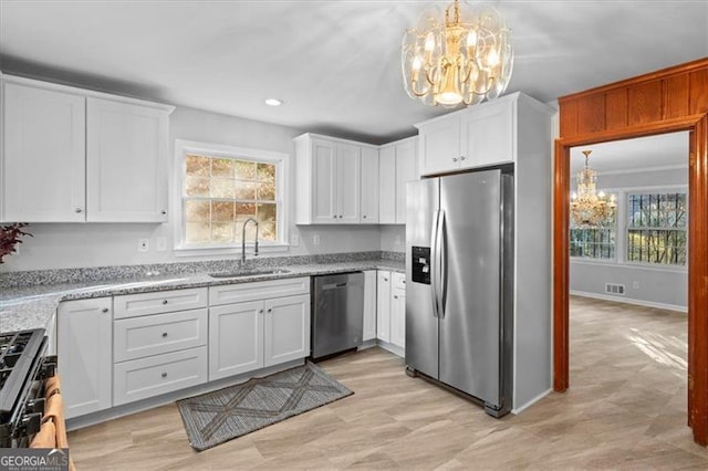 kitchen with a chandelier, stainless steel appliances, a sink, white cabinetry, and a healthy amount of sunlight