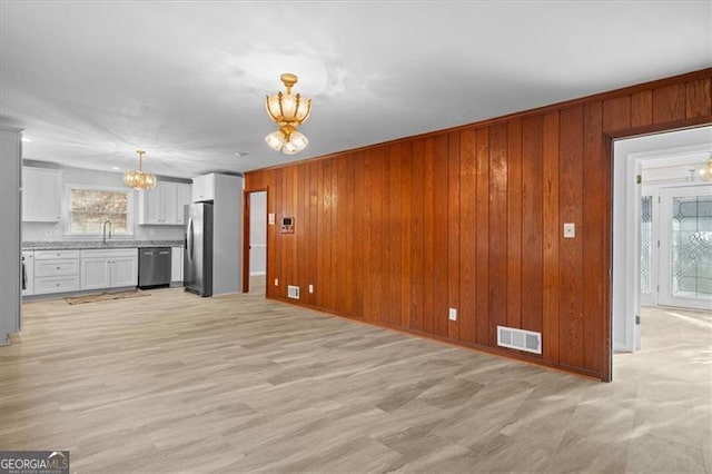 unfurnished living room with a notable chandelier, visible vents, light wood-style flooring, a sink, and wooden walls