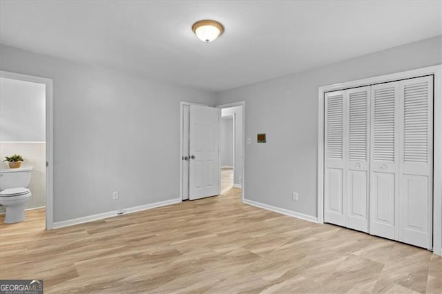 unfurnished bedroom featuring a closet, baseboards, light wood finished floors, and ensuite bathroom