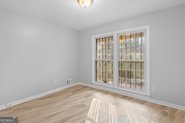 unfurnished room with light wood-style floors, a wealth of natural light, visible vents, and baseboards