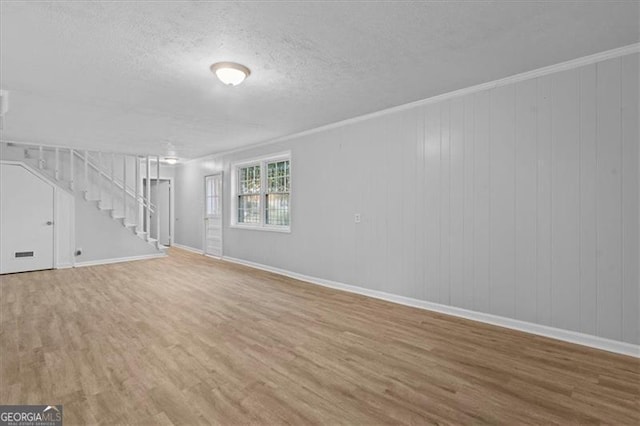 unfurnished living room featuring a textured ceiling, stairway, wood finished floors, and crown molding