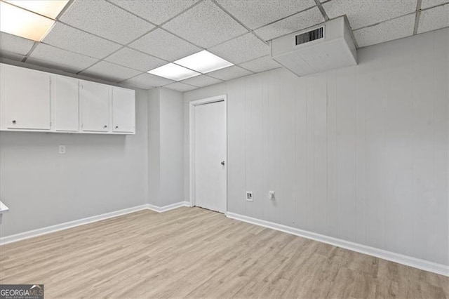 below grade area with a paneled ceiling, light wood-style floors, baseboards, and visible vents