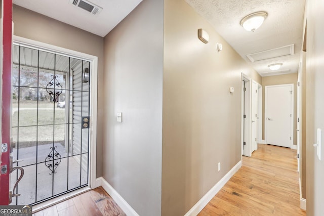 foyer entrance with a textured ceiling, wood finished floors, visible vents, and baseboards