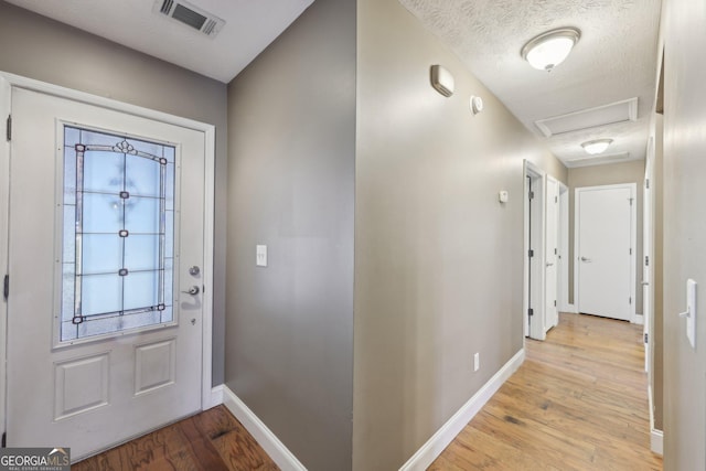 foyer entrance featuring baseboards, a textured ceiling, visible vents, and wood finished floors