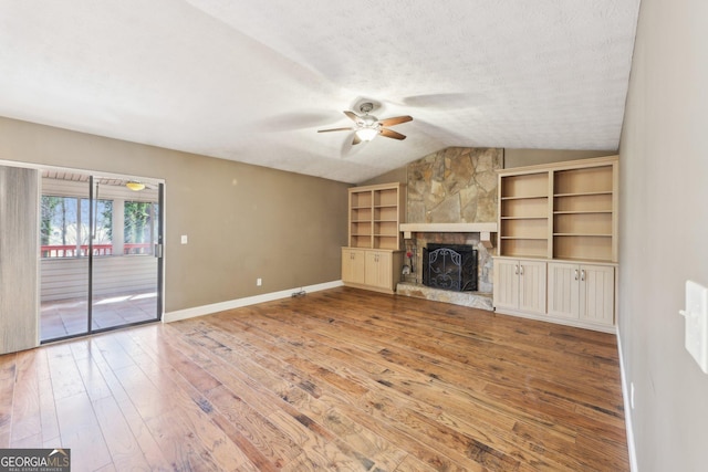 unfurnished living room featuring lofted ceiling, a textured ceiling, a fireplace, baseboards, and light wood-type flooring