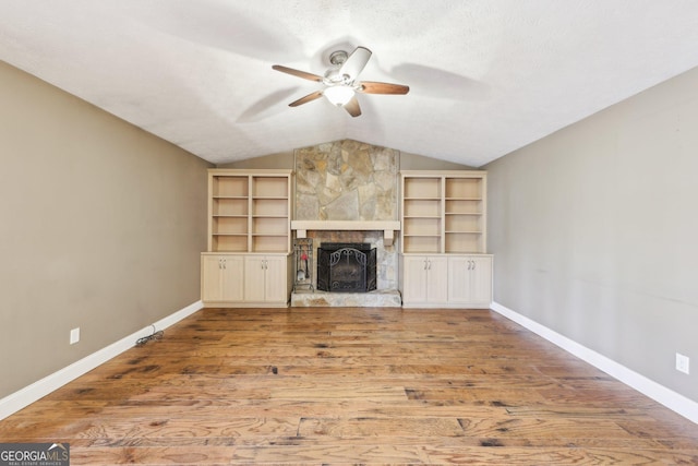 unfurnished living room with lofted ceiling, a stone fireplace, wood finished floors, a ceiling fan, and baseboards