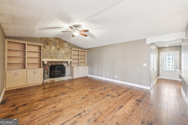 unfurnished living room with ceiling fan, a stone fireplace, hardwood / wood-style flooring, baseboards, and vaulted ceiling