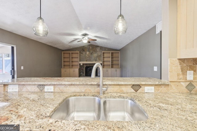 kitchen featuring light stone counters, lofted ceiling, a large fireplace, and a sink