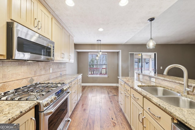 kitchen with light wood finished floors, baseboards, appliances with stainless steel finishes, a sink, and backsplash