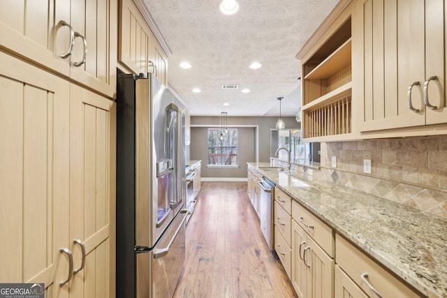 kitchen featuring decorative backsplash, appliances with stainless steel finishes, light wood-style floors, a sink, and a textured ceiling