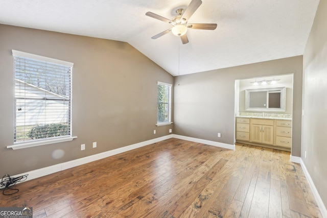 unfurnished bedroom featuring lofted ceiling, a ceiling fan, baseboards, light wood-type flooring, and ensuite bath