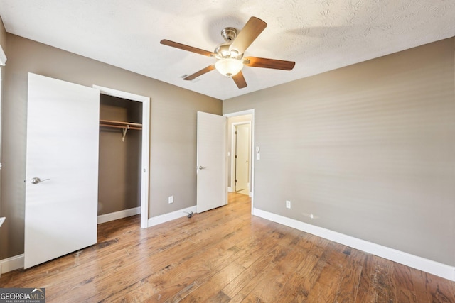 unfurnished bedroom featuring light wood finished floors, baseboards, a ceiling fan, a textured ceiling, and a closet