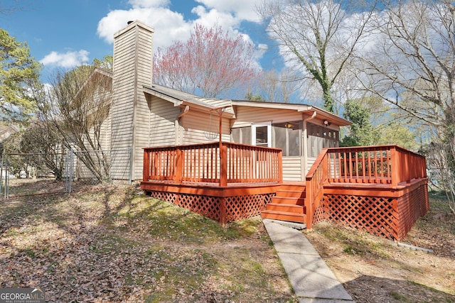 rear view of property with a chimney, a sunroom, fence, and a deck