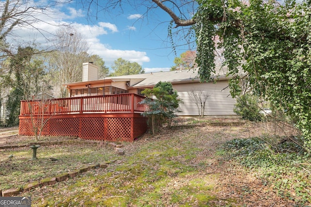 back of property featuring a deck, a chimney, and a sunroom