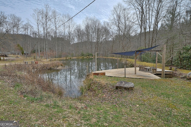 view of yard with a dock, a water view, and a forest view