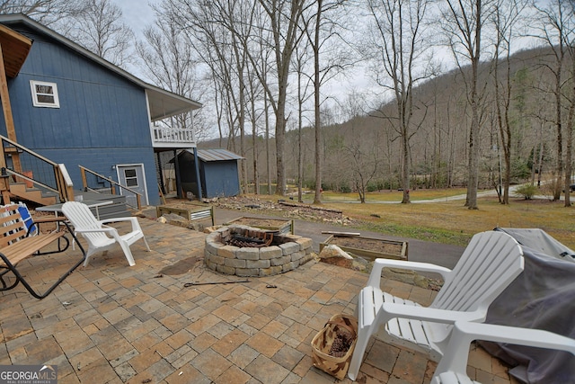 view of patio with an outbuilding, an outdoor fire pit, stairs, a storage unit, and a wooded view