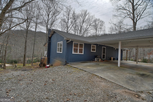 view of home's exterior featuring a carport, concrete driveway, and a shingled roof