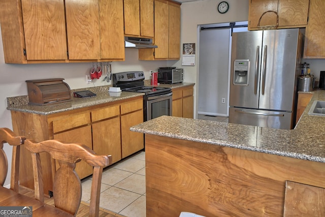 kitchen with light tile patterned floors, stainless steel appliances, brown cabinets, and under cabinet range hood