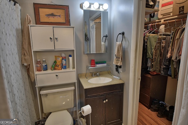 full bathroom with toilet, a spacious closet, wood finished floors, and vanity