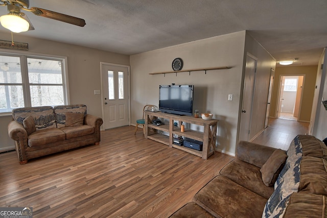 living area with a textured ceiling, ceiling fan, wood finished floors, visible vents, and baseboards