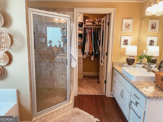 bathroom with a spacious closet, wood finished floors, a shower stall, and vanity