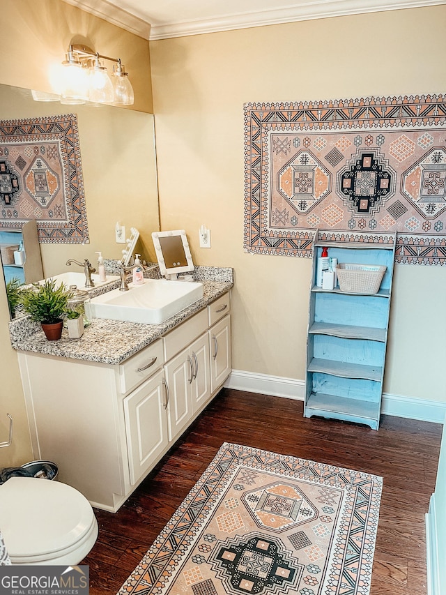 half bathroom with crown molding, vanity, baseboards, and wood finished floors