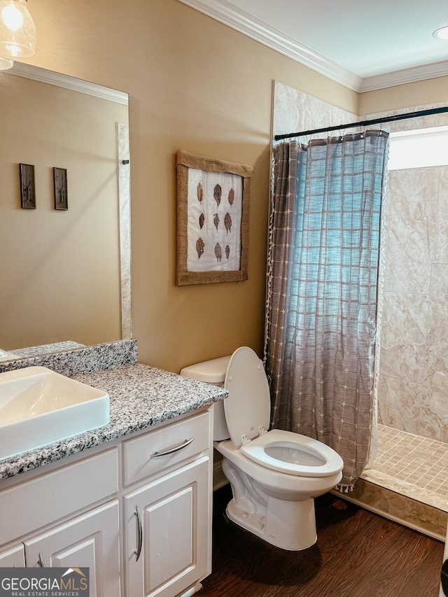 bathroom with crown molding, toilet, a tile shower, vanity, and wood finished floors